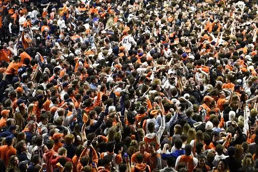 Fans storm the court at the conclusion of a college basketball game in Champaign, Ill., on Sunday, March 6, 2022. After about two months of falling COVID-19 cases, pandemic restrictions have been lifted across the U.S., and many people are taking off their masks and returning to indoor spaces. (AP Photo/Michael Allio)