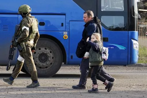 CAPTION CORRECTS THE LOCATION - A man and a girl who left a shelter in the Metallurgical Combine Azovstal walk to a bus escorting by a serviceman of Russian Army in Mariupol, in territory under the government of the Donetsk People's Republic, eastern Ukraine, Friday, May 6, 2022. (AP Photo/Alexei Alexandrov)