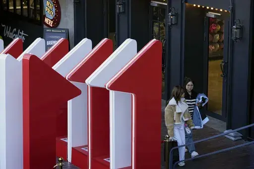 Women walk out from a fashion boutique near a display promoting the China popular e-commerce sales, the "Singles' Day" global online shopping festival, at a shopping mall in Beijing, on Nov. 4, 2024. (AP Photo/Andy Wong)