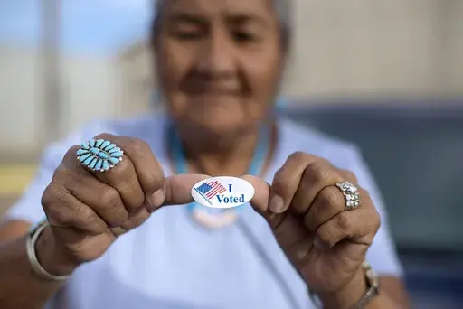 Mildred James of Sanders, Ariz., shows off her "I Voted" sticker as she waits for results of the Navajo Nation presidential primary election to be revealed in Window Rock, Ariz., Aug. 28, 2018. (AP Photo/Cayla Nimmo, File)