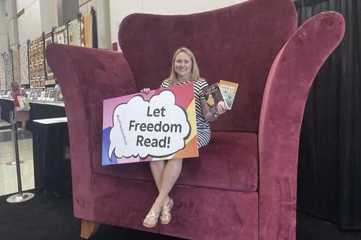 CORRECTS YEAR TO 2023 - School librarian Jamie Gregory, from South Carolina, displays two books that have been repeatedly challenged in the United States, while seated at the Banned Books from the Big Chair station at the American Library Association's annual conference in Chicago, June 24, 2023. The two books are: "Gender Queer," by Maia Kobabe, and "Out of Darkness," by Ashley Hope Pérez. (AP Photo/Claire Savage)
