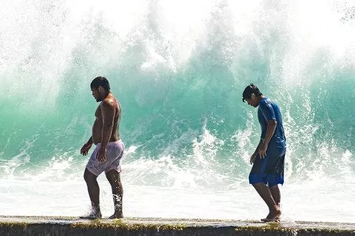 People walk in front of the high surf near Kapahulu Groin (Waikiki Wall) in Waikiki, Hawaii, Sunday, July 17, 2022. (Craig T. Kojima/Honolulu Star-Advertiser via AP)
