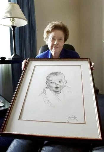 Ann Taylor Cook, poses at her Tampa, Fla., home Wednesday afternoon Feb. 4, 2004, with a copy of her photo that is used on all Gerber baby food products. Ann Turner Cook, whose cherubic baby face was known the world over as the original Gerber baby, has died. She was 95. Gerber announced Cook's passing in an Instagram post on Friday, June 3, 2022. (AP Photo/Chris O'Meara, File)